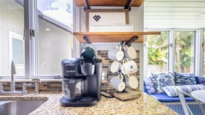 Une cuisine équipée d’une machine à café Keurig, d’un plan de travail en granit, d’un évier et d’une fenêtre donnant sur un paysage verdoyant.