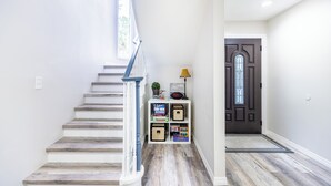 Un escalier avec une rampe blanche mène à un palier. On y trouve des boîtes de rangement et une porte ornée d’un panneau de verre décoratif.