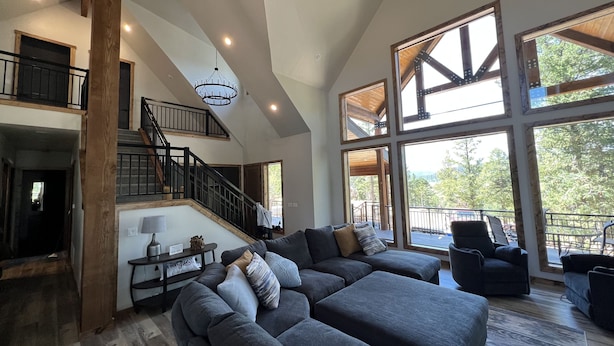 A spacious living area with a large sectional sofa, a staircase, and large windows offering a view of the outdoors.