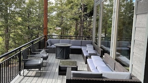 A covered deck with outdoor seating, large windows, and a view of trees.