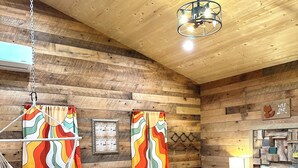 Une chambre confortable avec un plafond en bois, un fauteuil suspendu, un lit recouvert d’une courtepointe aux couleurs vives et une lampe fixée au mur.
