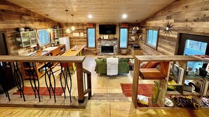 L’intérieur chaleureux d’un chalet, avec un revêtement mural en bois, un coin repas, un salon doté d’une cheminée et une cuisine avec une cheminée en pierre.