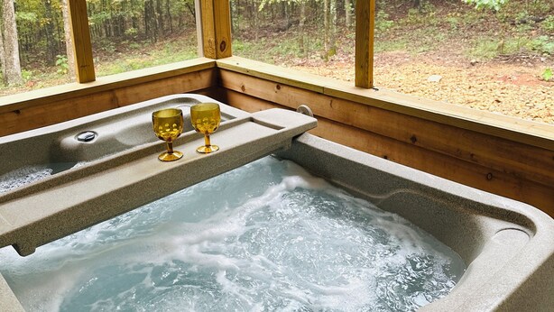 Un bain à remous avec un intérieur en bois et une vue sur une forêt, grâce à de grandes fenêtres.