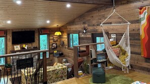 L’intérieur chaleureux d’un chalet avec un plafond en bois, un fauteuil suspendu, une cheminée et un téléviseur fixé au mur.