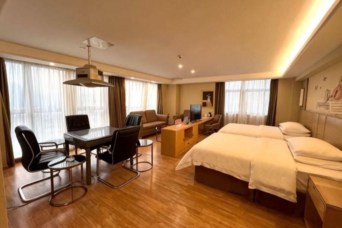 A hotel room with a bed, a desk with a computer, a chair, and a table.