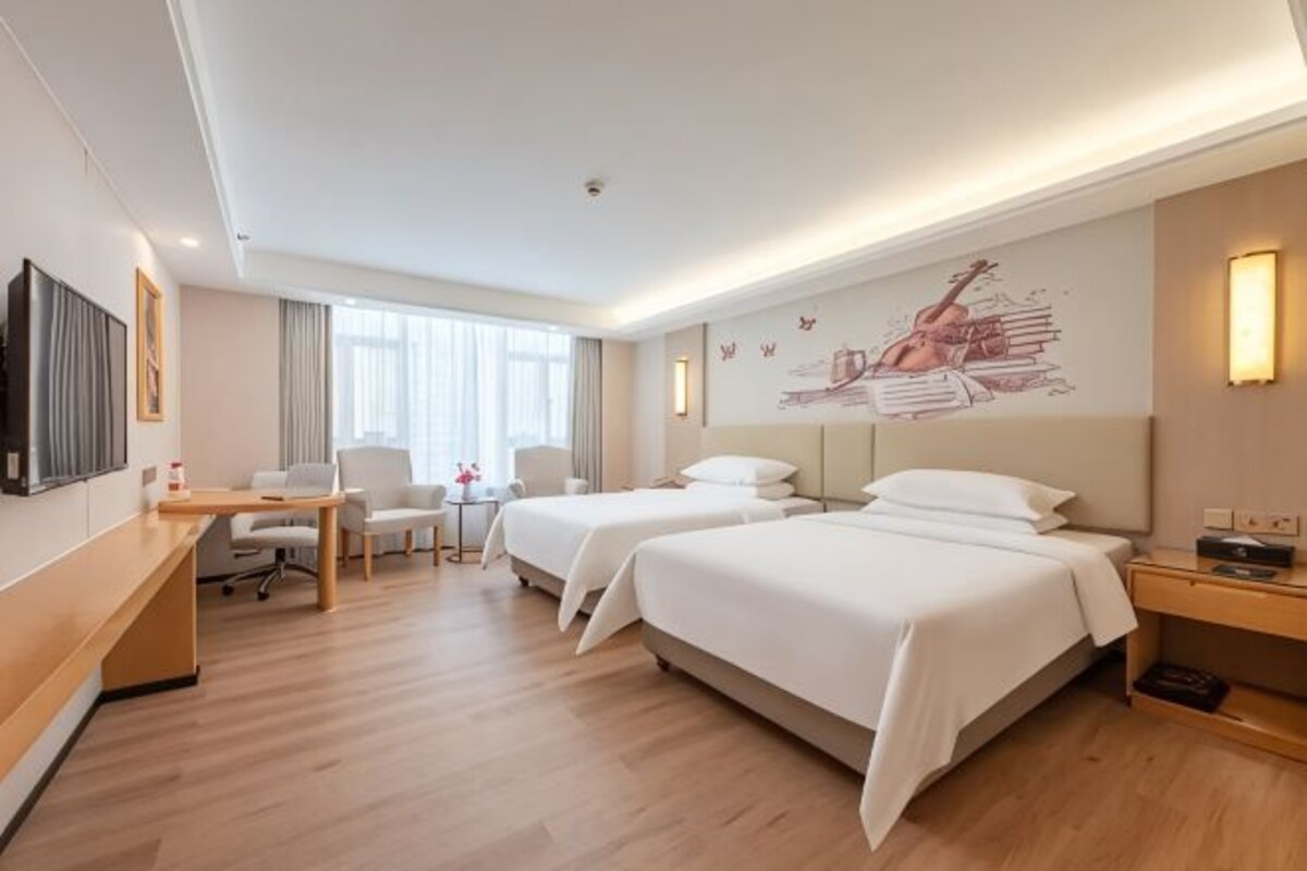 A hotel room with two beds, a desk, a chair, a TV, and a wall with a guitar artwork.