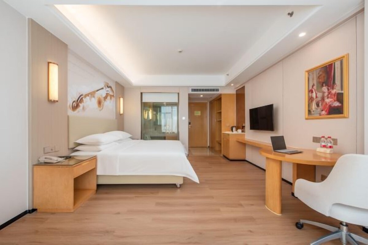 A hotel room with a bed, a desk, a chair, a TV, and a painting on the wall.