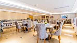 A spacious dining area with multiple tables and chairs, a buffet line with various dishes, and a television screen mounted on the wall. - Vienna International Hotel ( Shunde Jun'anBiguiyuan Golf Club） (Foshan)