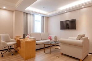 A modern hotel room with a sofa, a desk, a coffee table, and a flat-screen TV mounted on the wall. - Vienna International Hotel ( Shunde Jun'anBiguiyuan Golf Club） (Foshan)