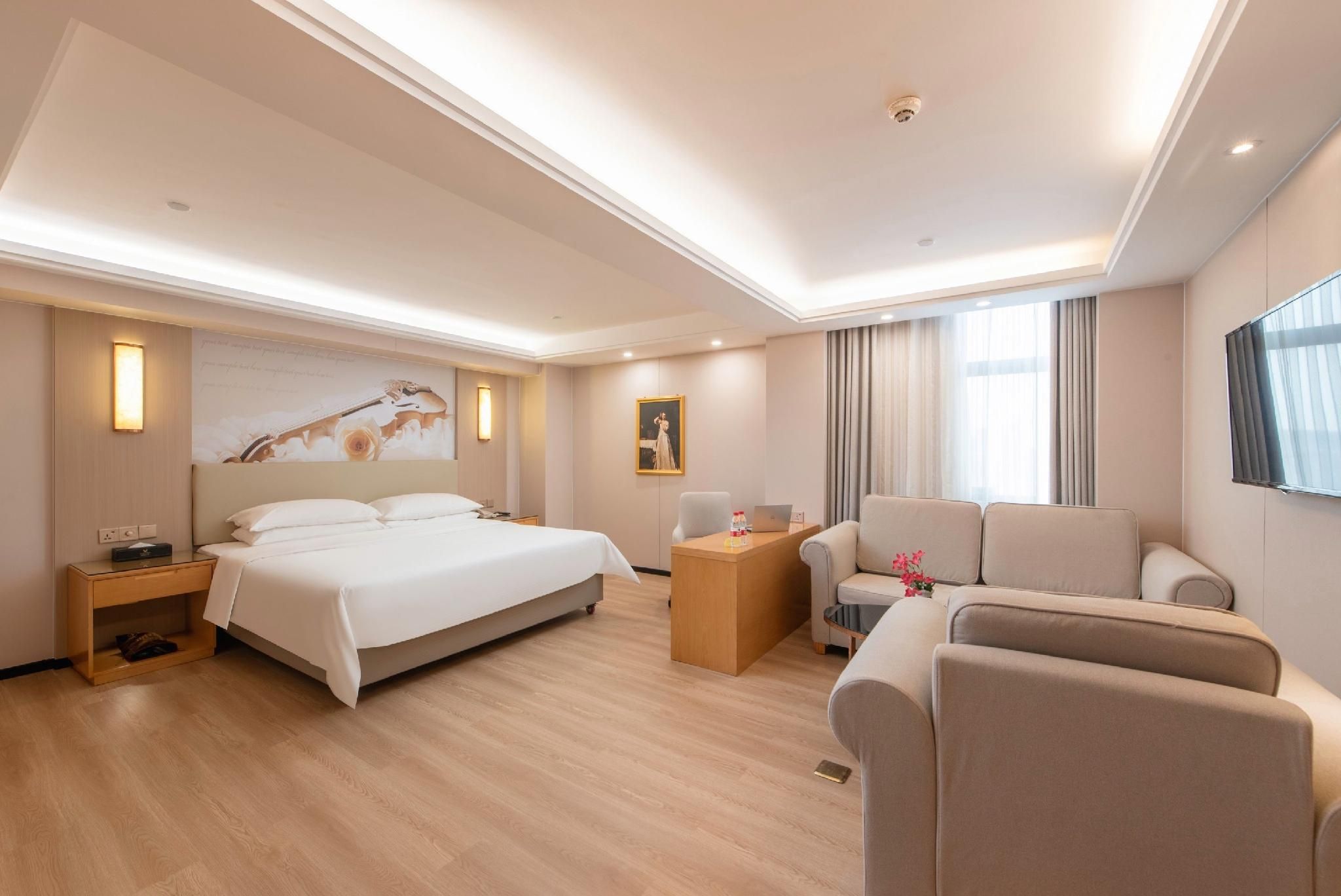 A hotel room with a bed, a desk, a chair, a sofa, and a TV.