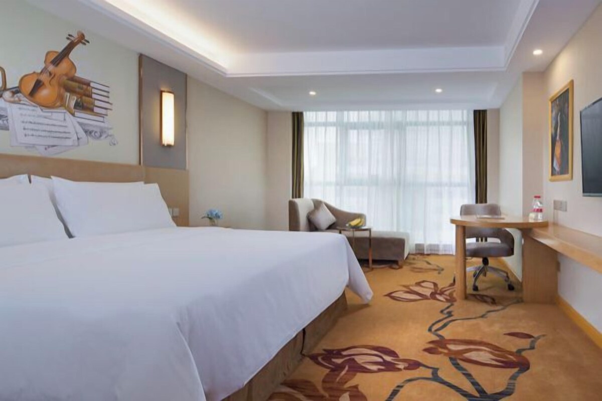 A hotel room with a large bed, a desk, a chair, and a window with curtains.