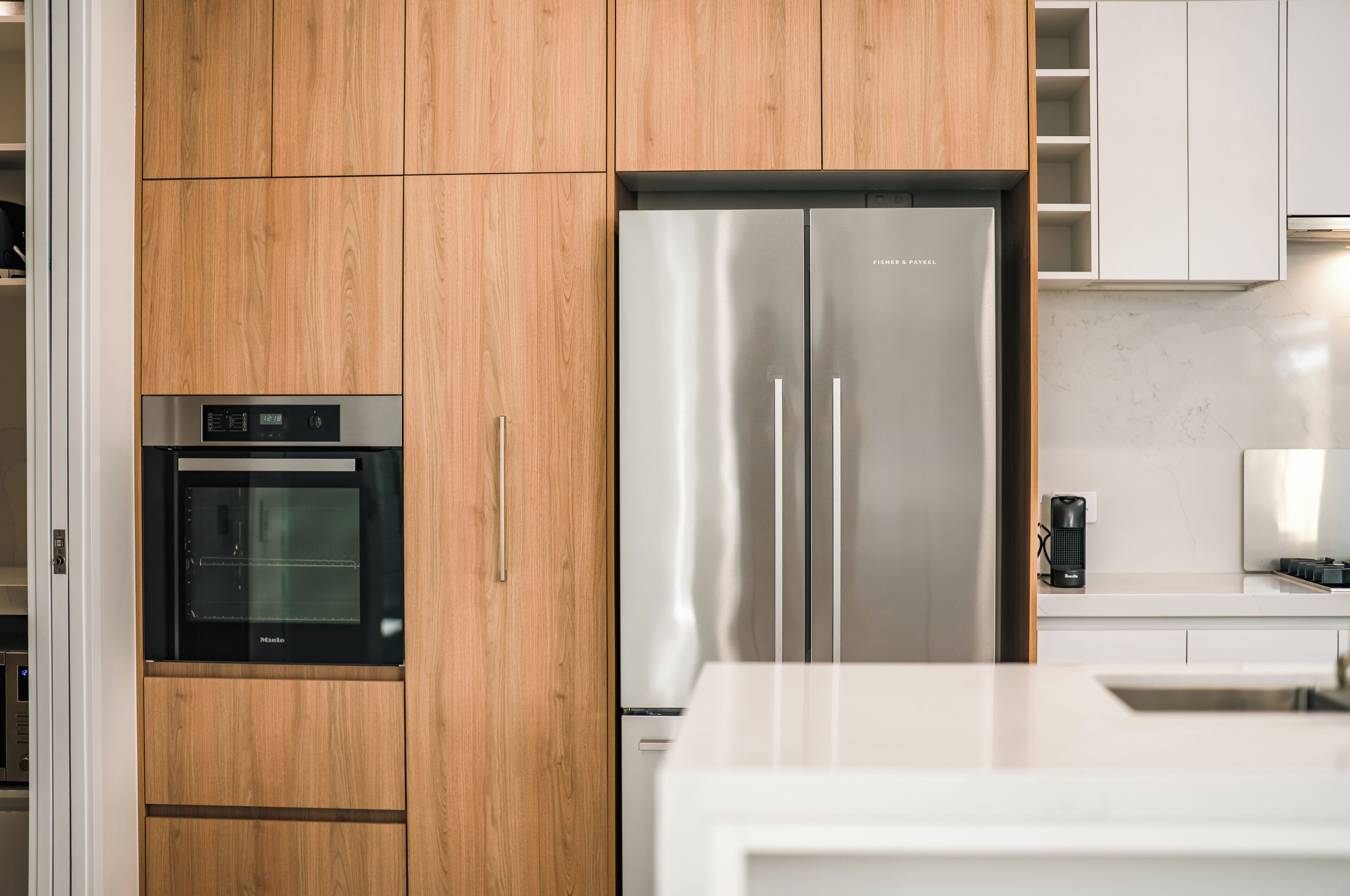 A kitchen with wooden cabinets, a stainless steel refrigerator, and a built-in oven.