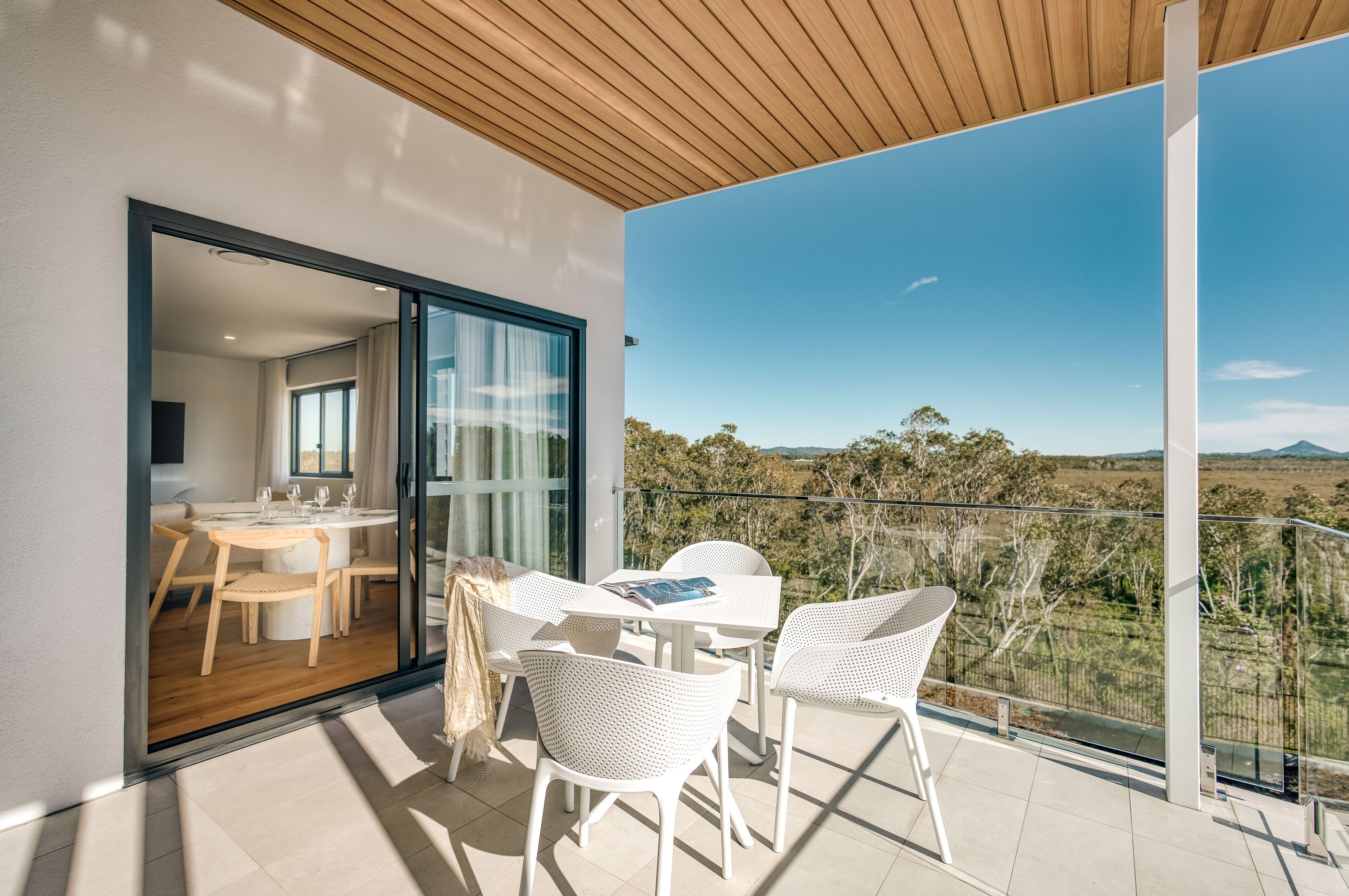 Un balcón moderno con sillas de mimbre blanco y una mesa, con vistas a un paisaje pintoresco.