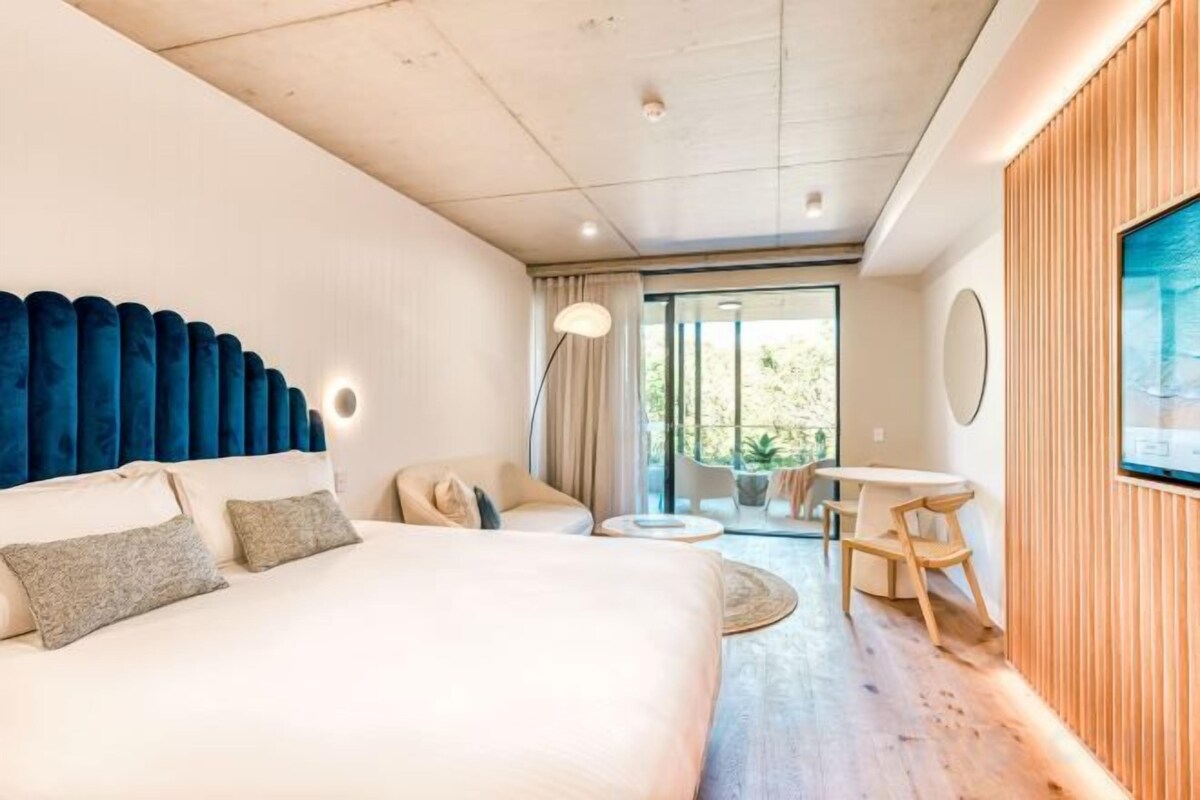 Una habitación de hotel con una cama grande, un espacio de descanso con una mesa redonda y vistas al exterior.