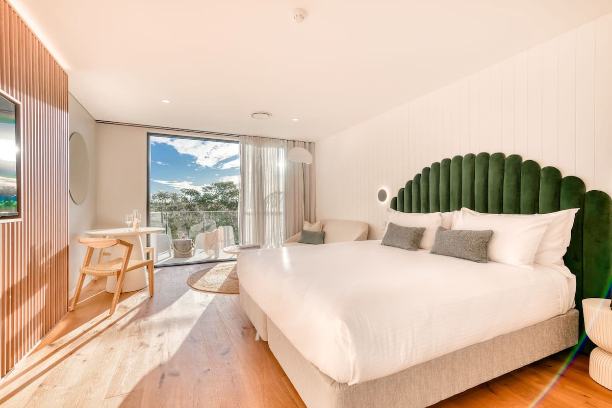 A modern bedroom with a large bed, a small table, and a view of the outdoors.