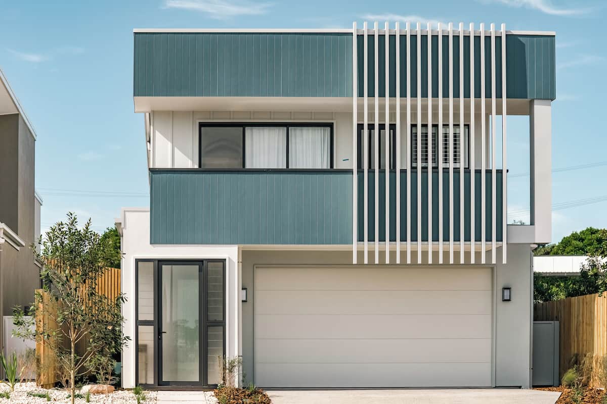 A modern two-story house with a garage, a balcony, and a wooden fence.