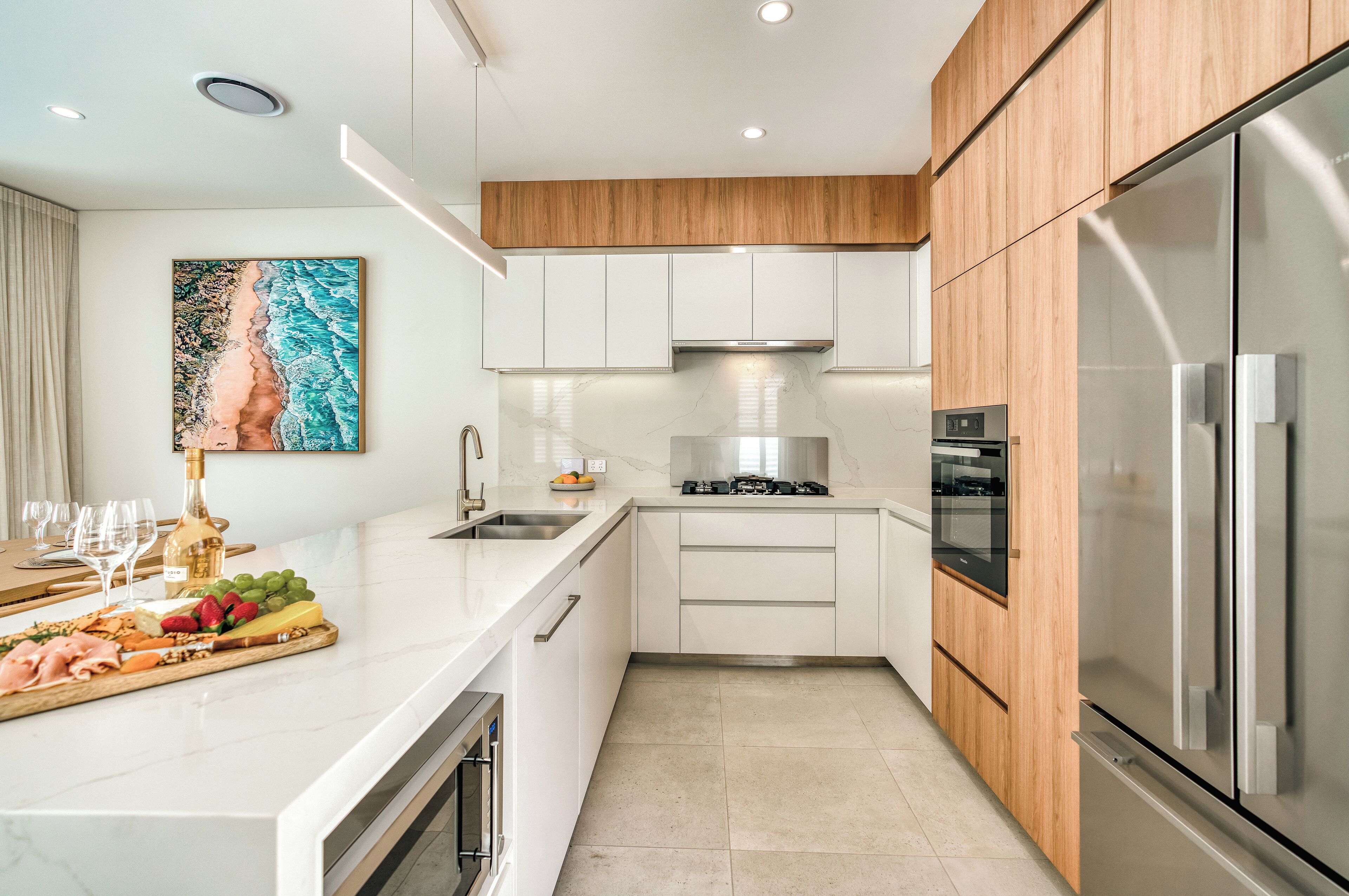 Une cuisine moderne avec des meubles blancs, un élément supérieur en bois, des appareils en acier inoxydable et un plan de travail en marbre.