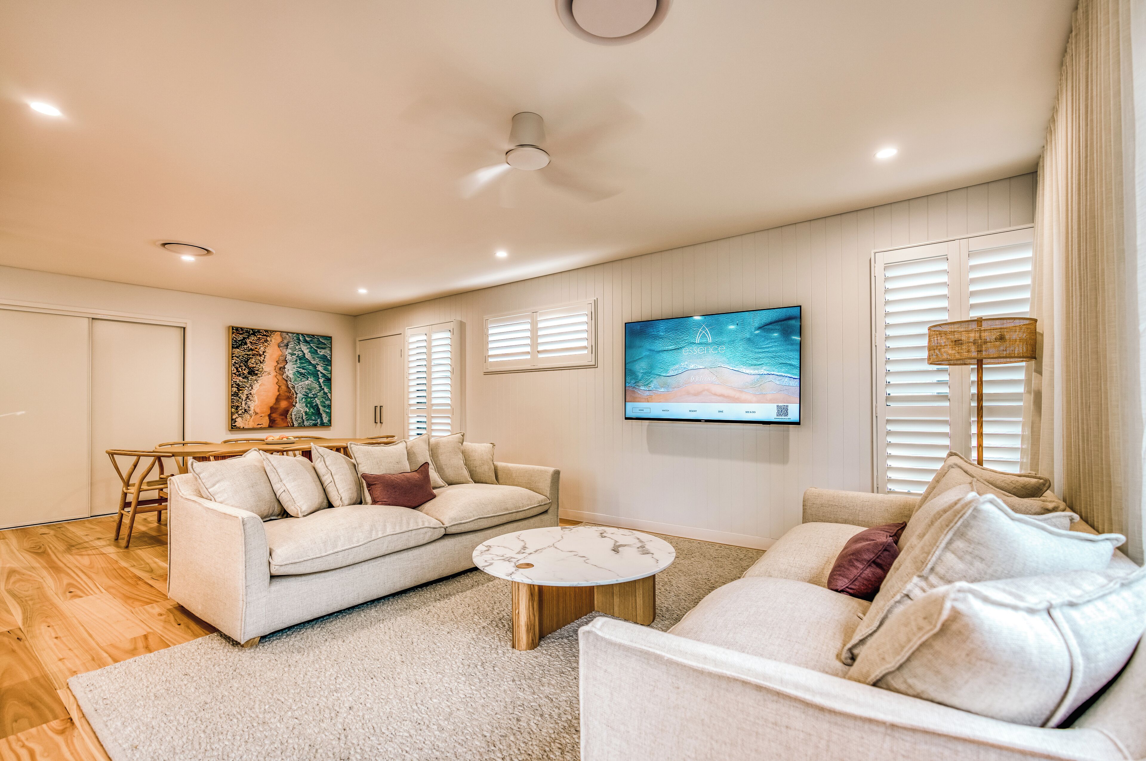 A modern living room with a sofa, armchair, coffee table, and a flat-screen TV mounted on the wall.