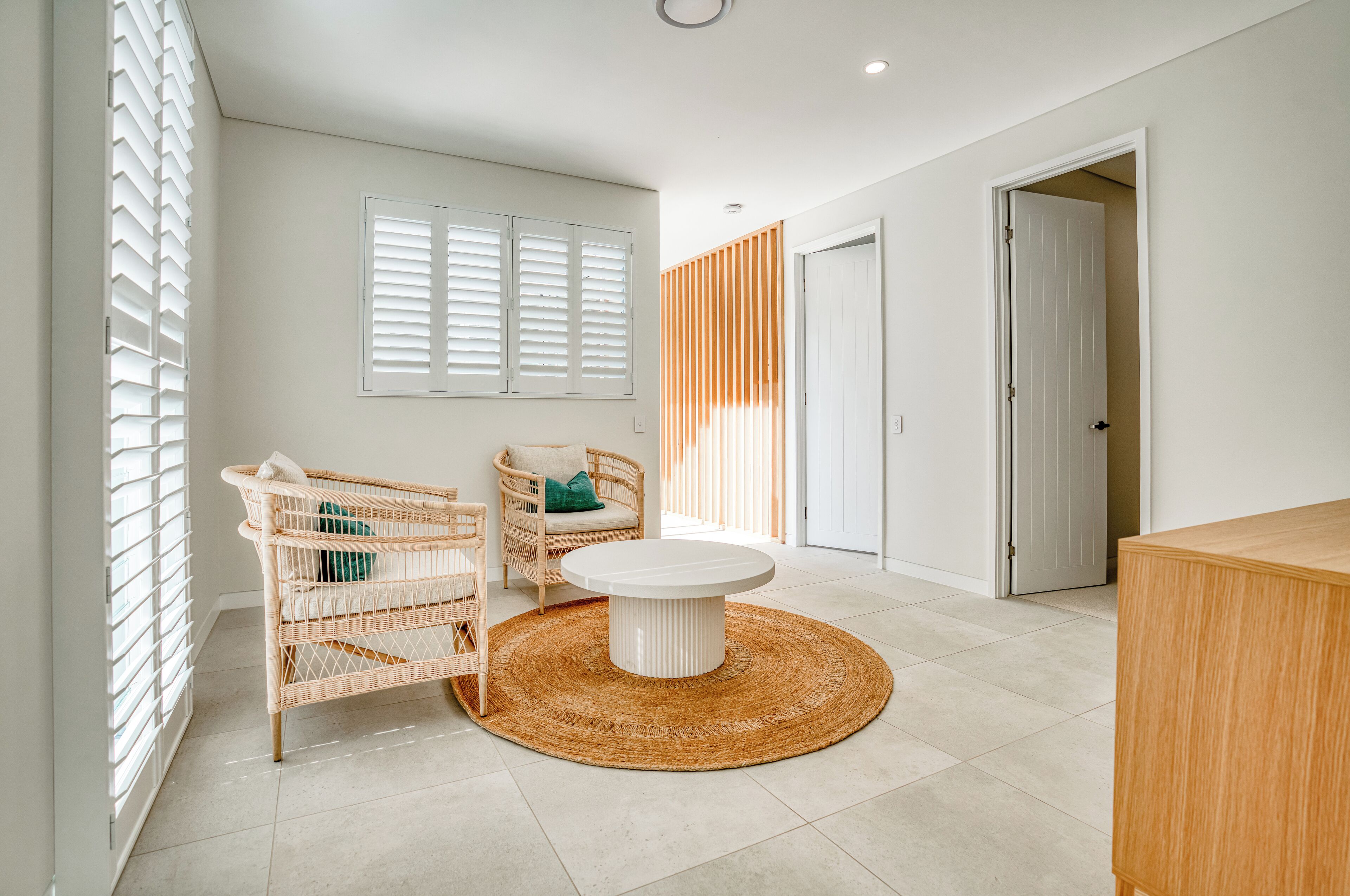 A spacious room with a round table, wicker chairs, a woven rug, and a door leading to another room.