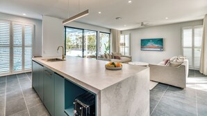 Una cocina moderna con una isla central, un área de comedor con sofá y ventanas amplias con persianas.