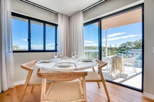 Uma área de refeições com uma mesa redonda para quatro pessoas, grandes janelas e vista para o exterior.