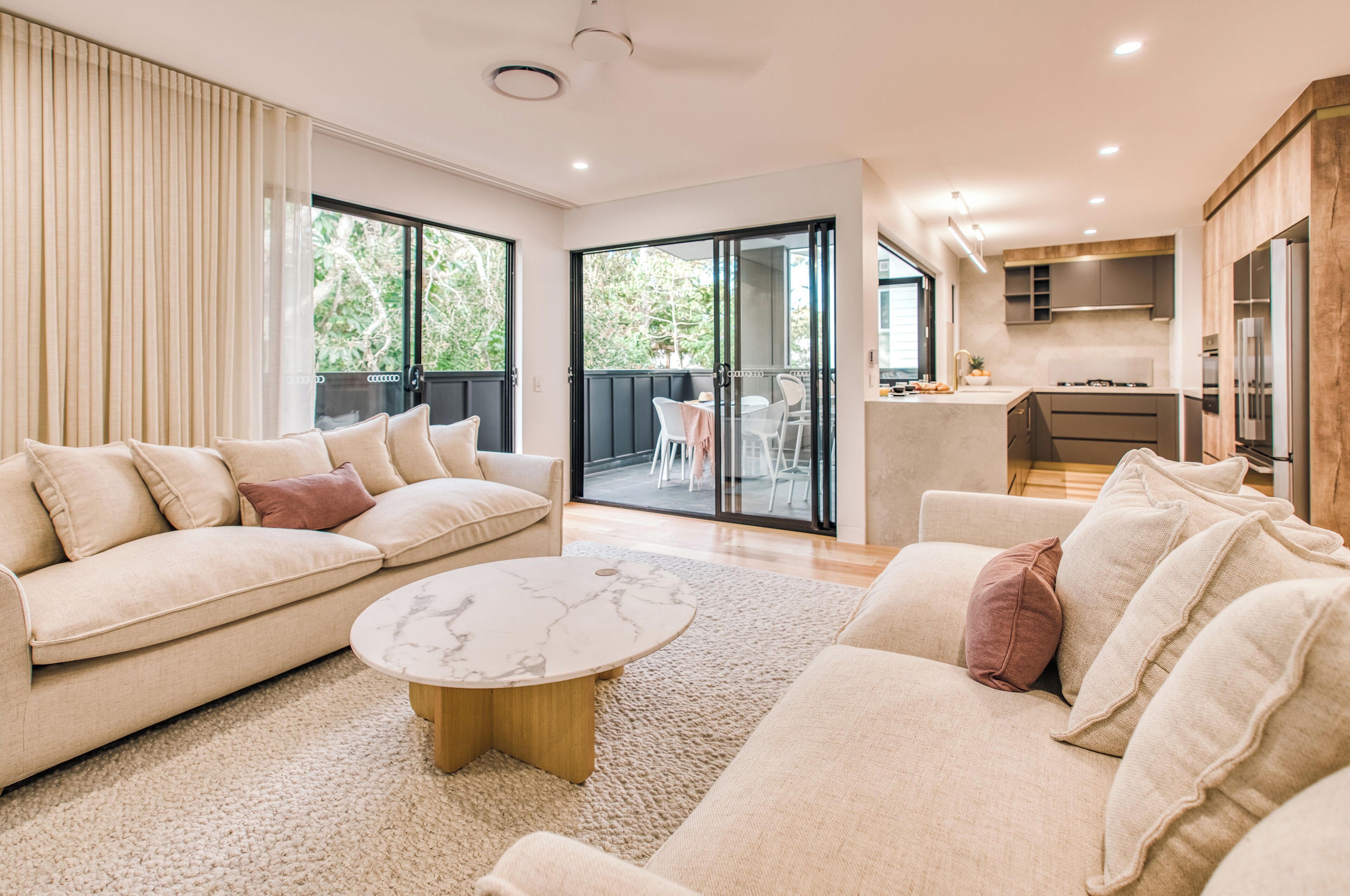 A modern living room with a beige sofa, a round coffee table, and a sliding glass door leading to a balcony.