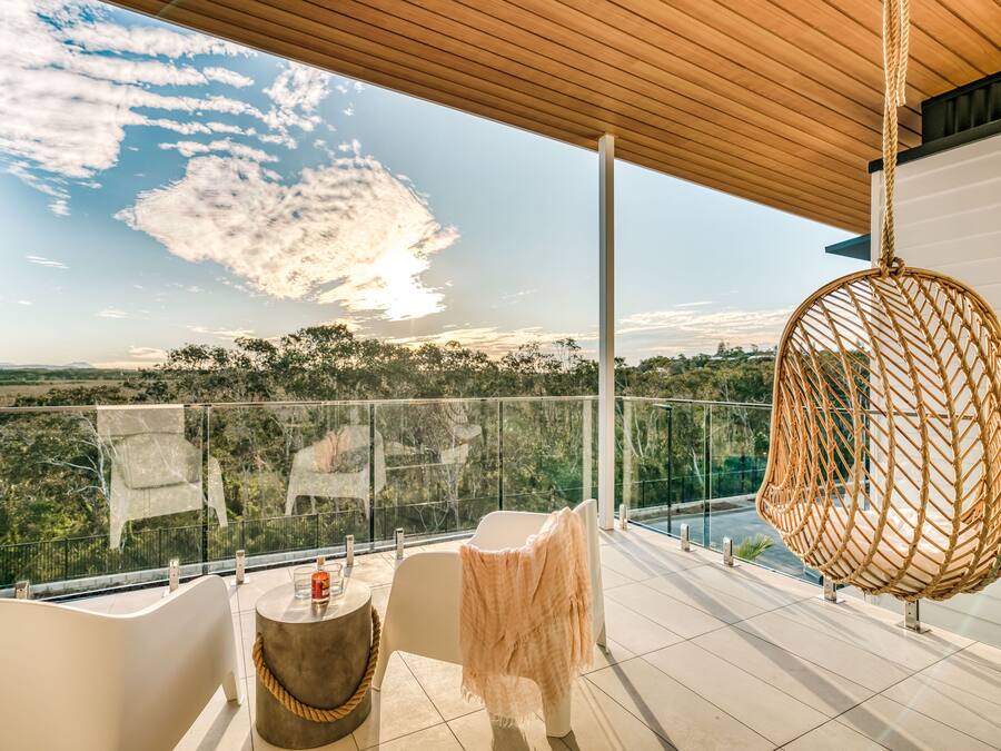 A balcony with a view of a landscape, a hanging chair, and a table with a bottle.