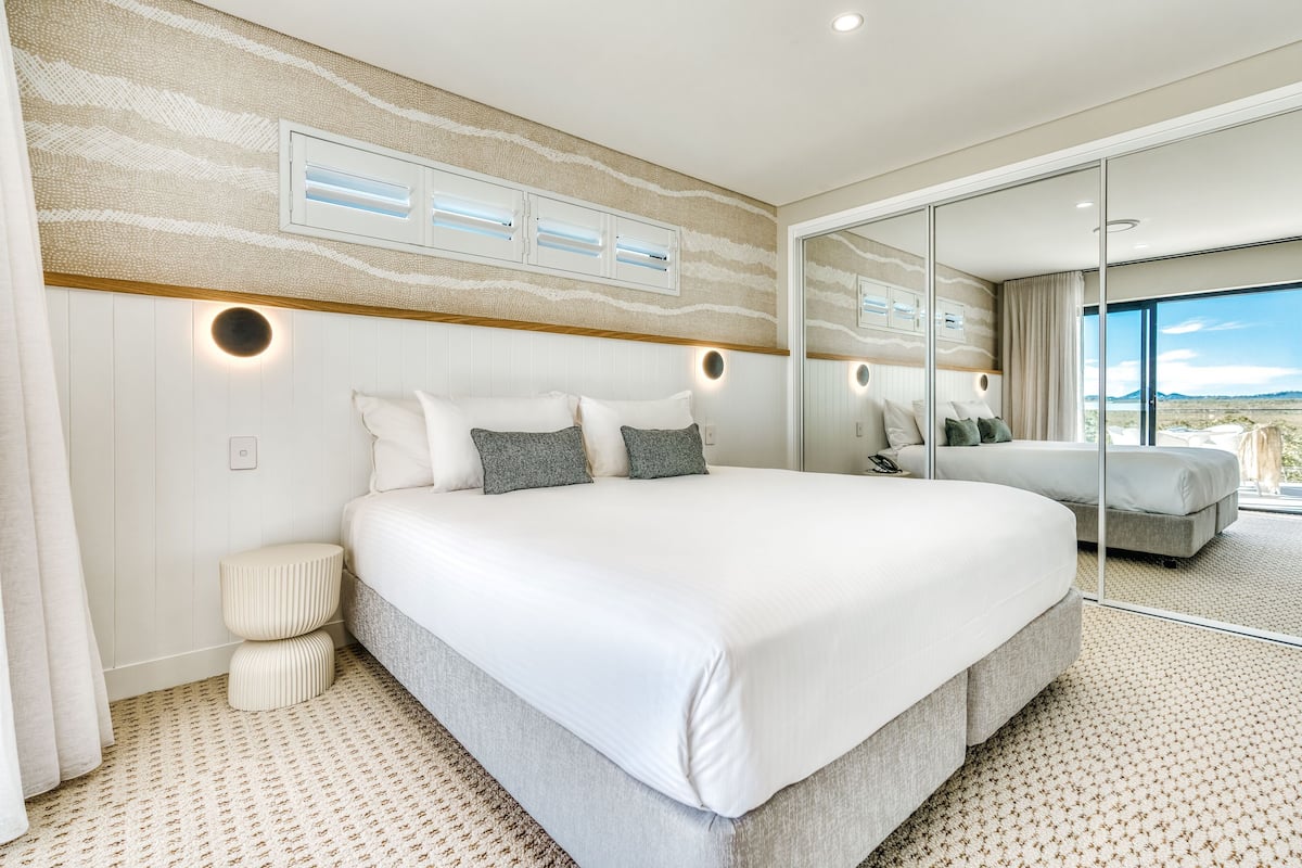 A large bed with white bedding, a round bedside table, and a wall-mounted light fixture.
