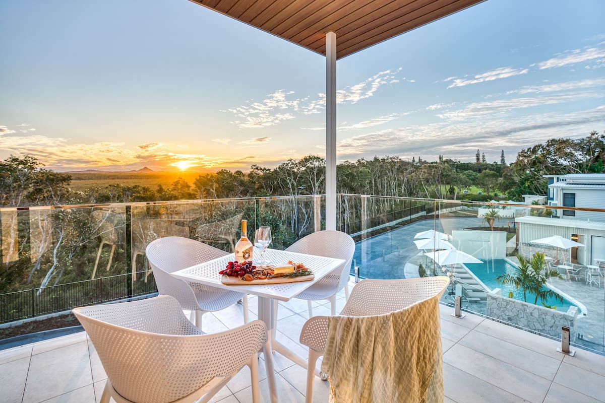 A terrace with a table set for two, overlooking a swimming pool and a scenic landscape during sunset.