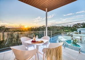 Una terraza con una mesa preparada para dos, con vistas a una piscina y un paisaje pintoresco al atardecer.