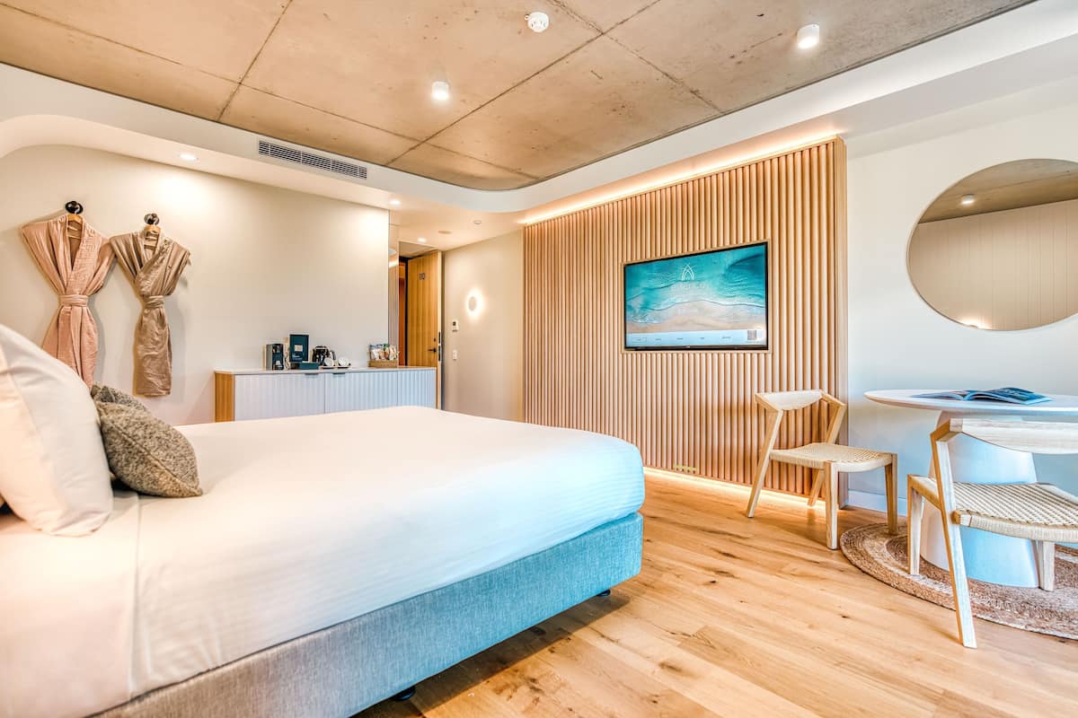 A modern hotel room with a large bed, a desk with a chair, a TV, and a wooden panel wall.