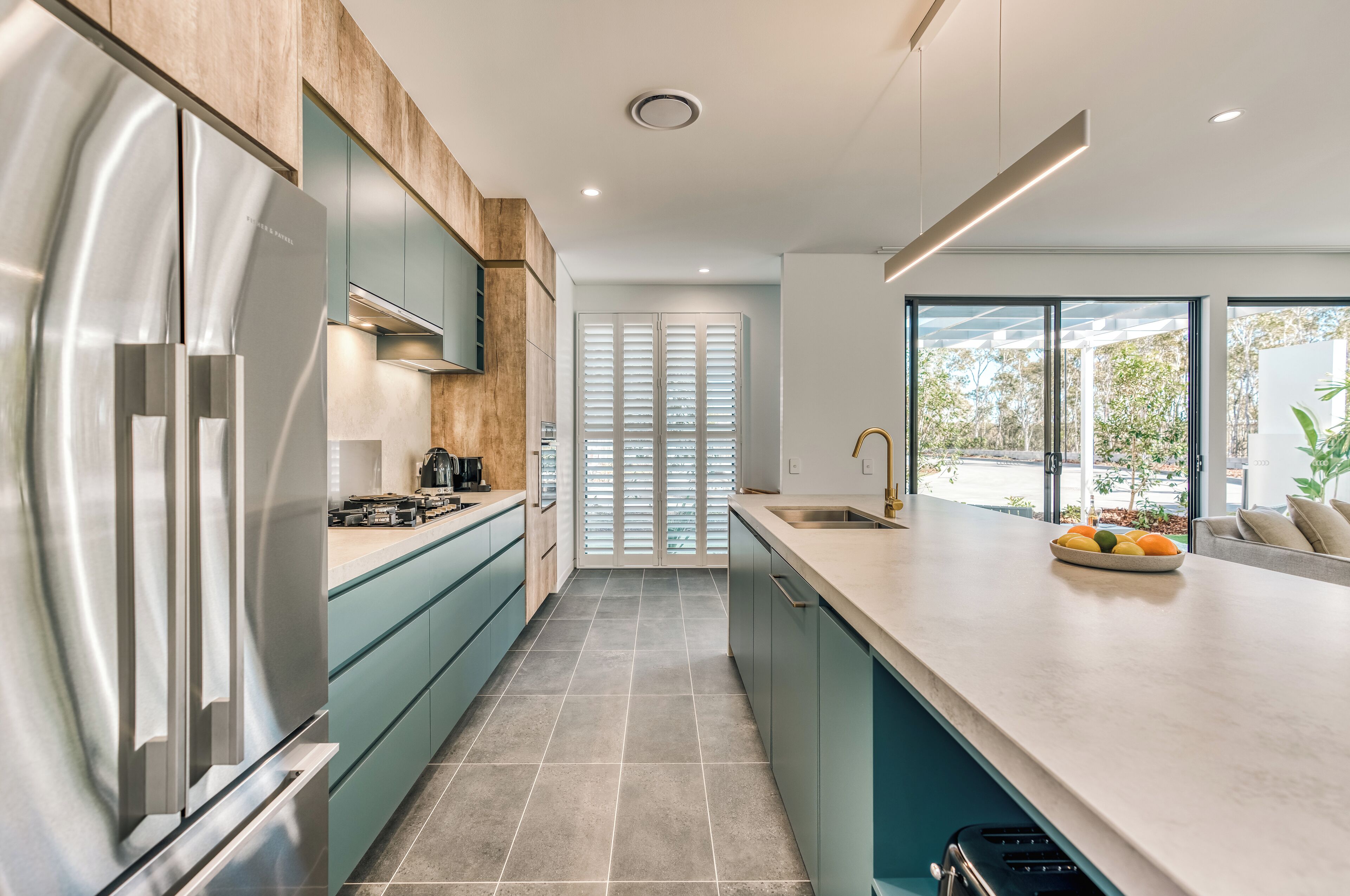 Una cucina moderna con elettrodomestici in acciaio inossidabile, mobili color petrolio e un'ampia finestra che permette l'illuminazione naturale.