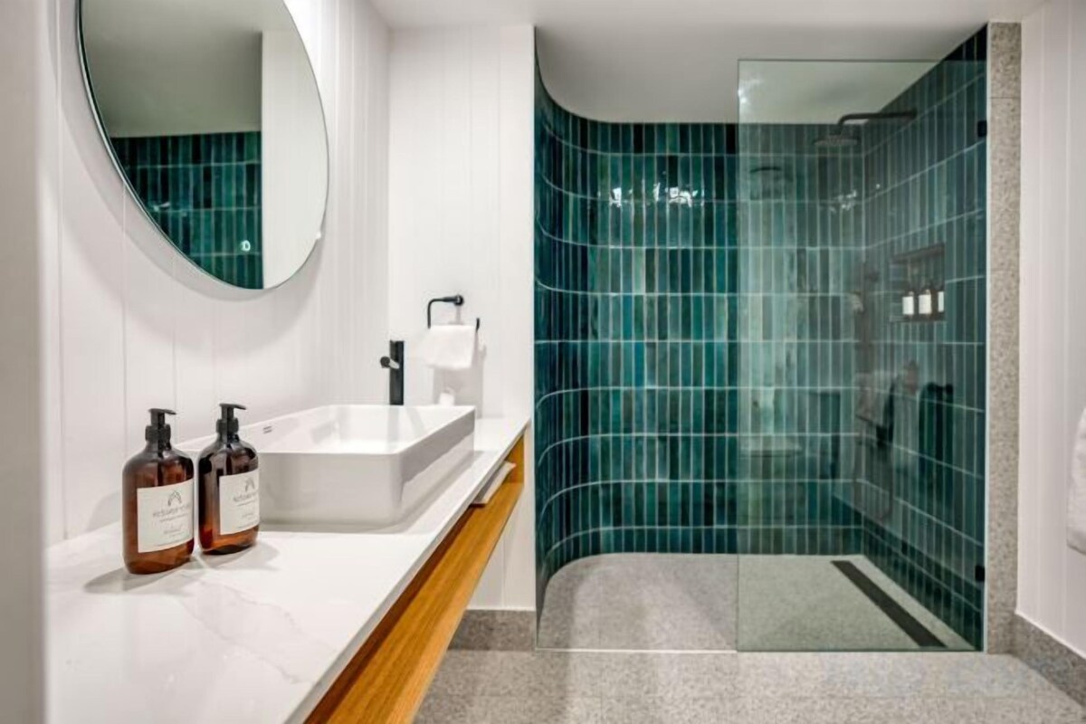 Un bany modern amb un lavabo blanc, un mirall rodó i una cabina de dutxa de vidre.