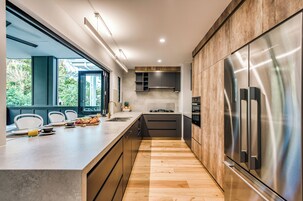 Een moderne keuken met een centraal eiland, roestvrijstalen apparatuur en uitzicht op groen.