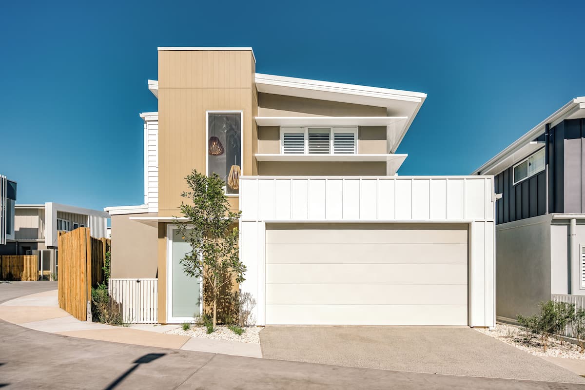A modern two-story house with a garage, a wooden fence, and a small tree in the front yard.
