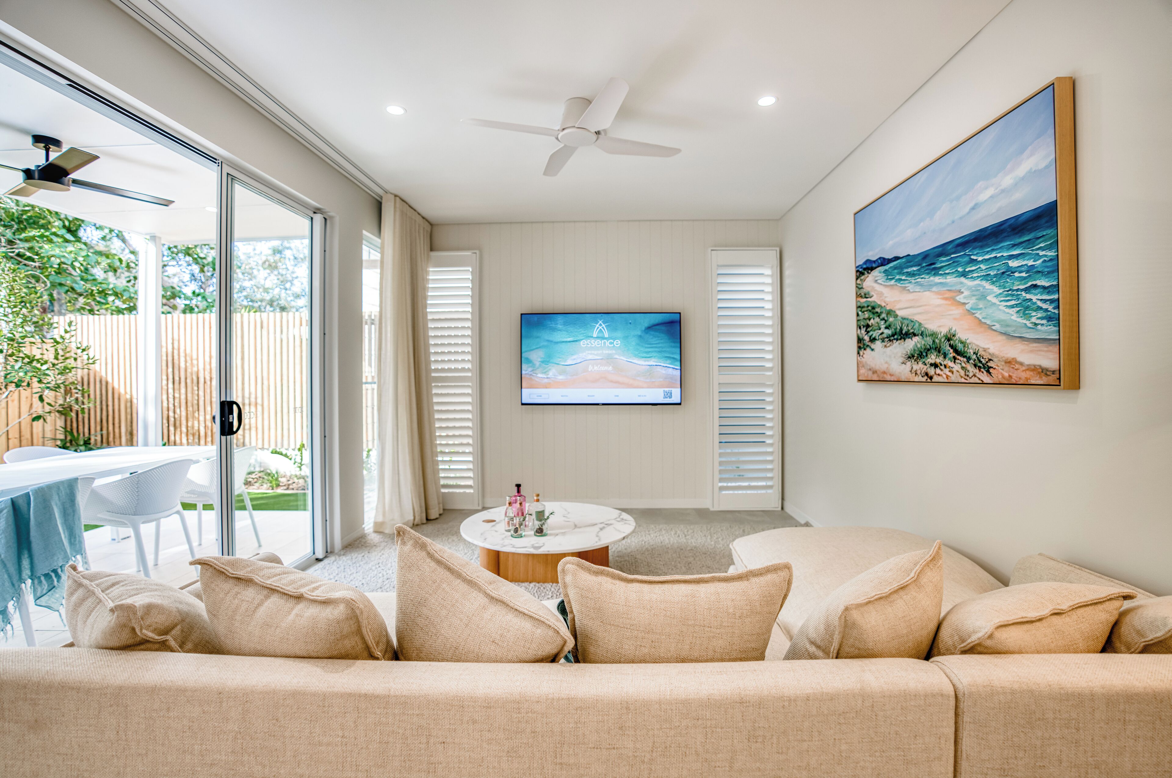 A modern living room with a beige sofa, a round coffee table, and a flat-screen TV mounted on the wall.