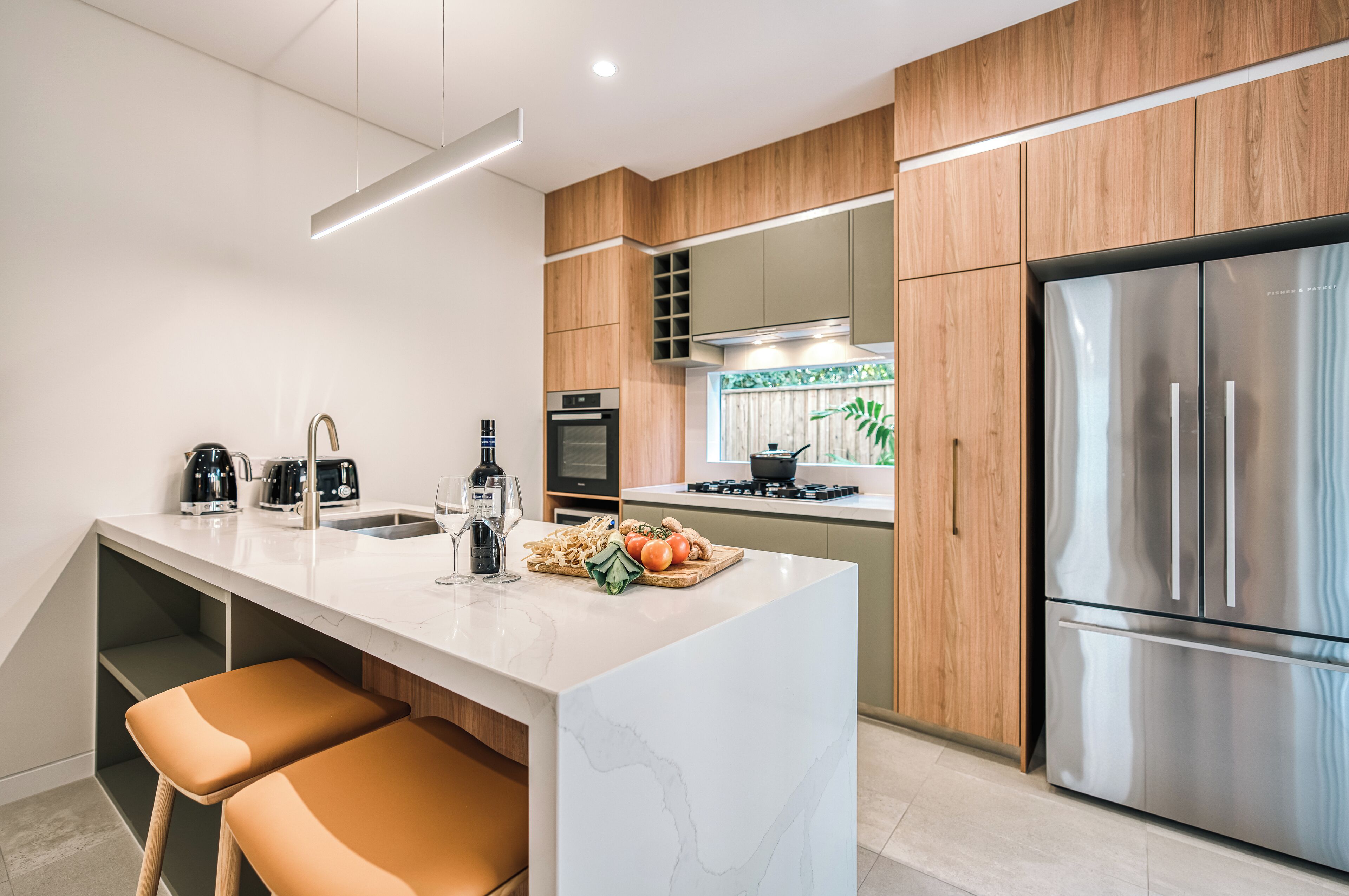 Une cuisine moderne dotée d’un îlot en marbre, de meubles en bois, d’appareils électroménagers en acier inoxydable et de deux tabourets de bar marron.