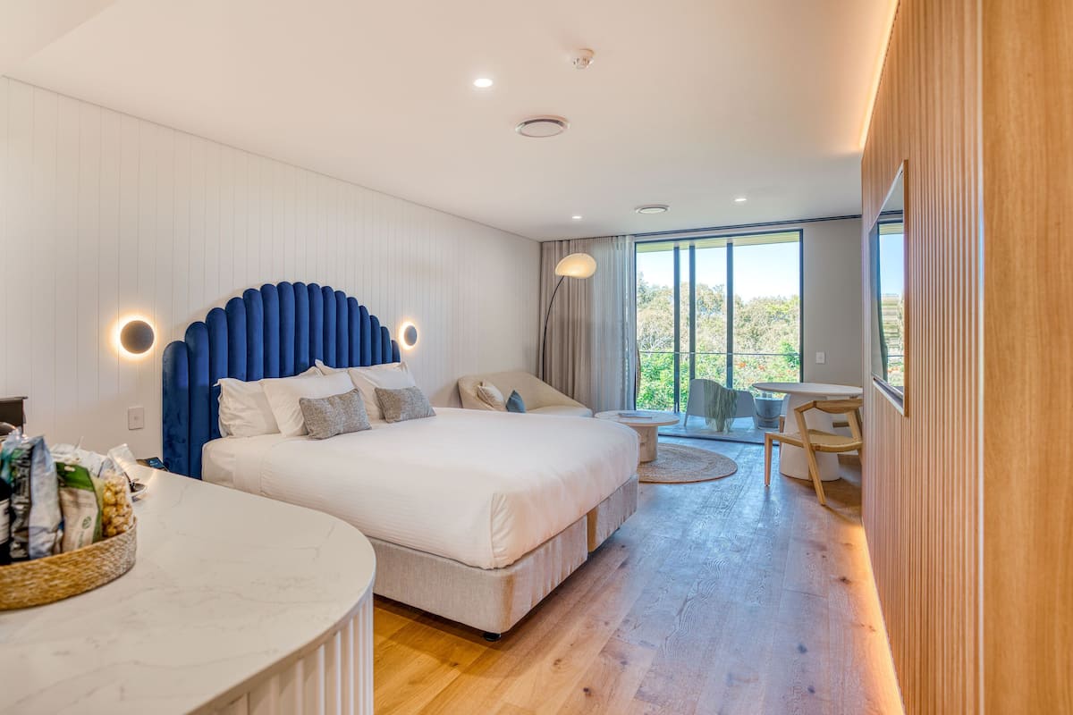 A modern bedroom with a large bed, a desk, and a balcony.