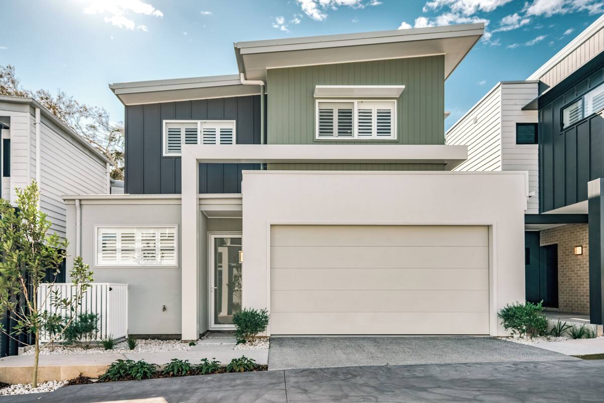 A modern two-story house with a garage, a front porch, and a small garden area.