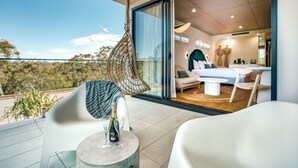 Una habitación moderna con una cama, un sofá y una mesa de comedor. Hay un balcón con una silla colgante y una botella de vino.