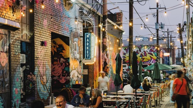 A bustling street scene with outdoor seating, graffiti on buildings, and string lights.