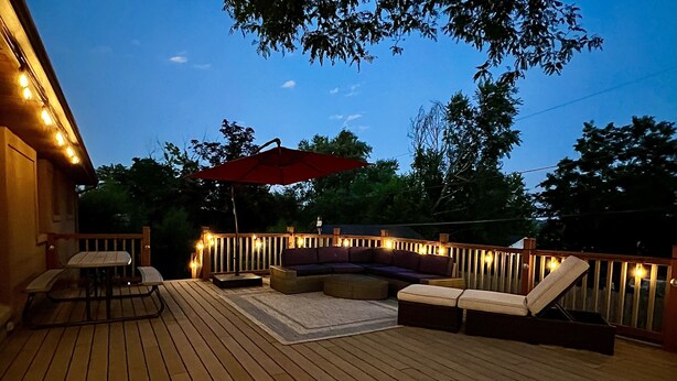 Um deck de madeira com um sofá curvo, uma mesa de jantar e um guarda-sol.