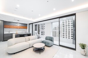 A modern living room with a sofa, armchair, and coffee table, a kitchen with wooden cabinets, and a large window offering a city view. - Seocho Intoraon Hotel and Residence (Seoul)