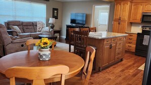 A modern kitchen with wooden cabinets, a dining area with a round table and chairs, a ceiling fan, and a TV in the background. - Discover Maryville and the Great Smoky Mountains (Maryville)