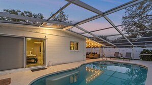 A poolside area with a covered patio, a glass door leading to a room, and outdoor seating. - Bahama Breeze | Private Pool w/ Patio + Outdoor TV! (Sarasota)