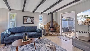 A modern living room with a stone fireplace, a blue sofa, and a television displaying a scenic view. - Bahama Breeze | Private Pool w/ Patio + Outdoor TV! (Sarasota)