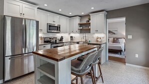 A modern kitchen with white cabinets, stainless steel appliances, and a wooden island with bar stools. - Bahama Breeze | Private Pool w/ Patio + Outdoor TV! (Sarasota)