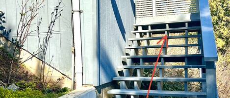 Un escalier en béton, doté d’une rampe métallique, mène à un immeuble à la façade grise.