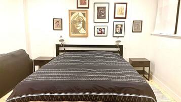 Een slaapkamer met een bed, twee nachtkastjes, een zwart hoofdeinde en kunstwerken in lijsten aan de muur.