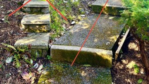 Eine Steintreppe führt einen Hügel hinauf, im Hintergrund ein Haus.